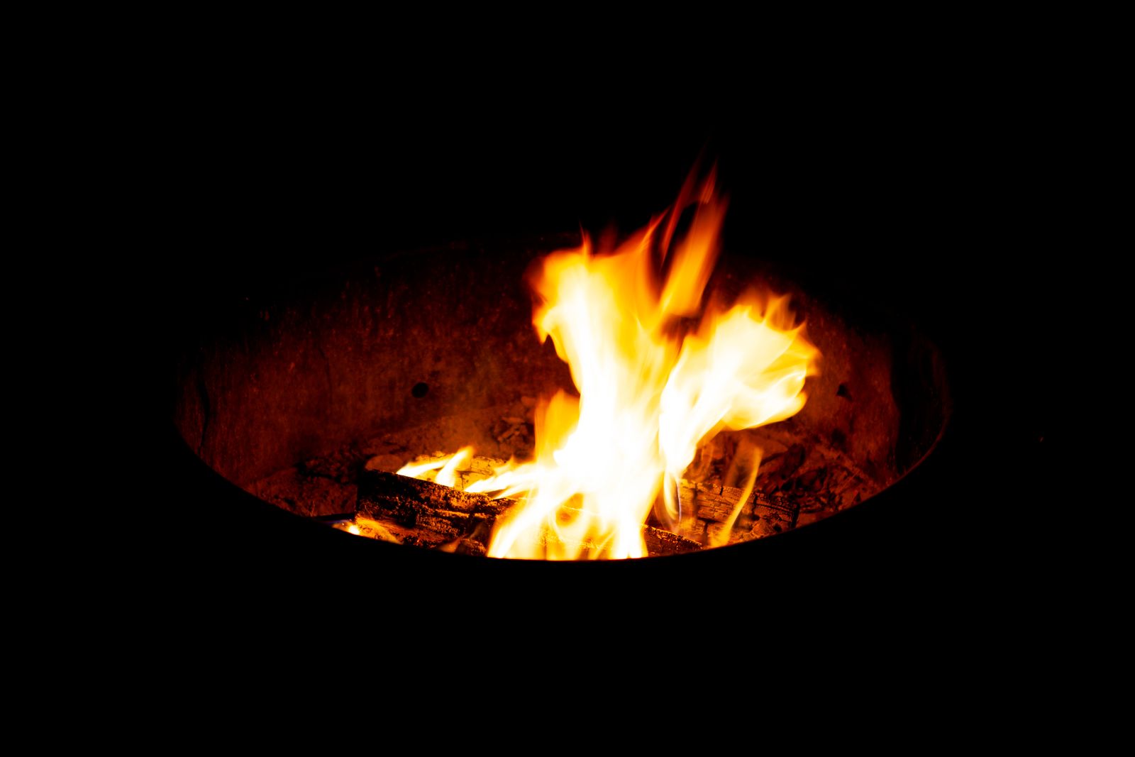 Close-up flames burning inside a round black steel fire pit at night