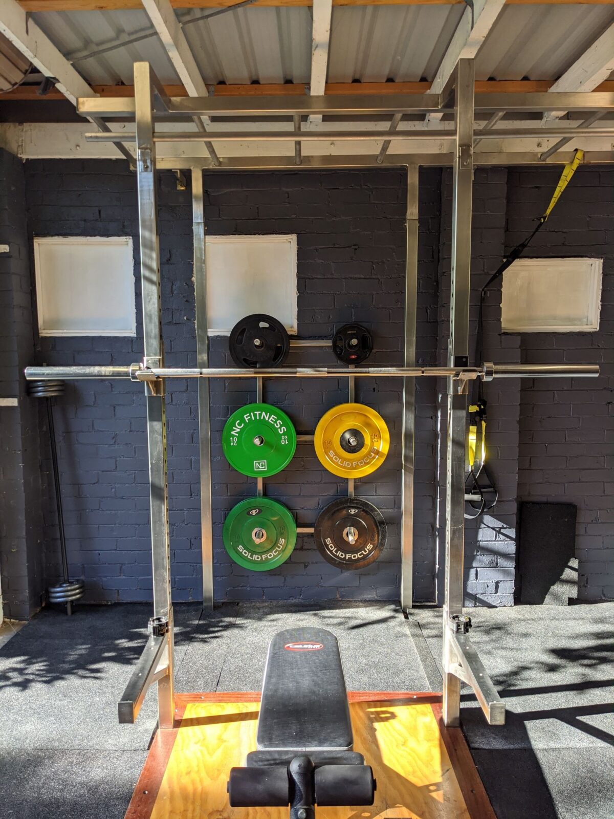 A squat rack set up in a home garage gym next to weight plates and a barbell