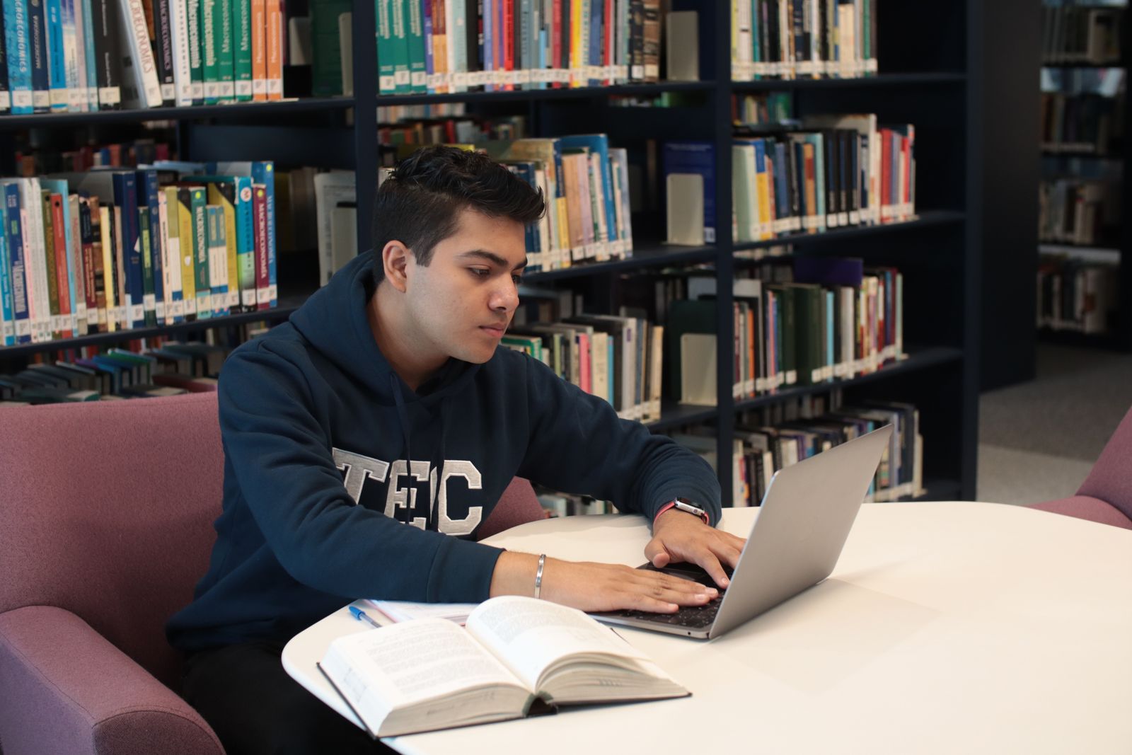 Student sitting in a library studying with a laptop and books