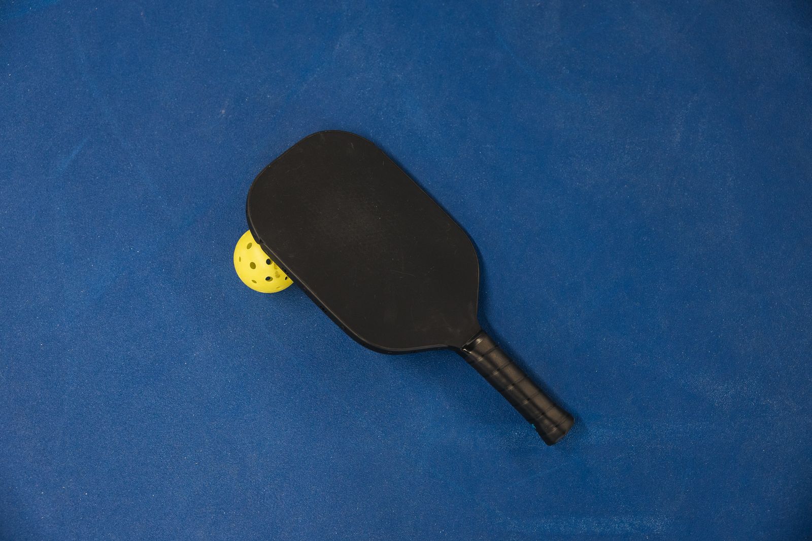 Pickleball paddle and ball resting on a blue court surface