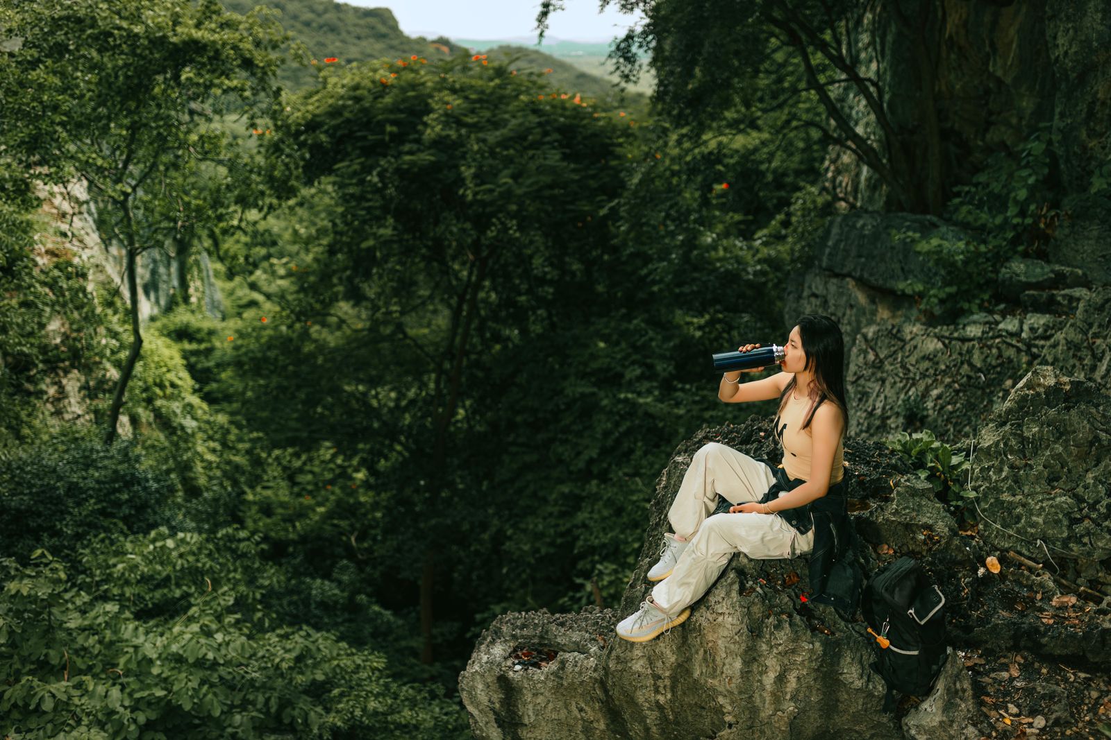 A hiker drinking water while sitting on a cliff