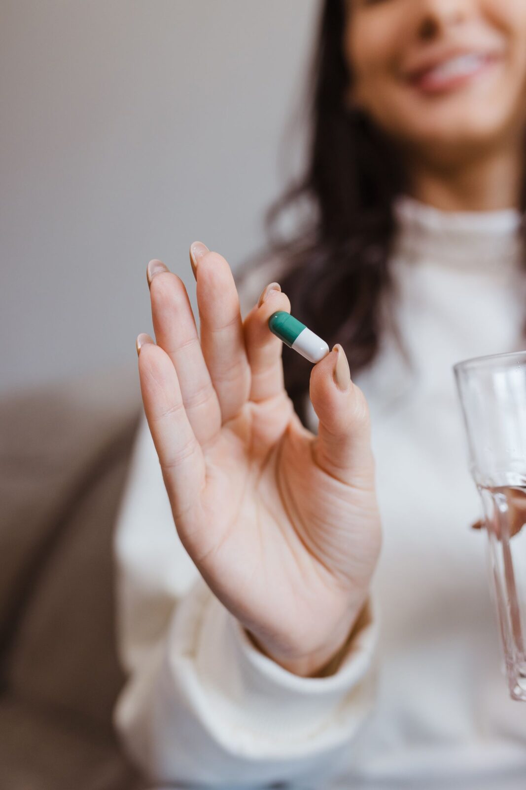 Hand holding a supplement capsule with a glass of water at night