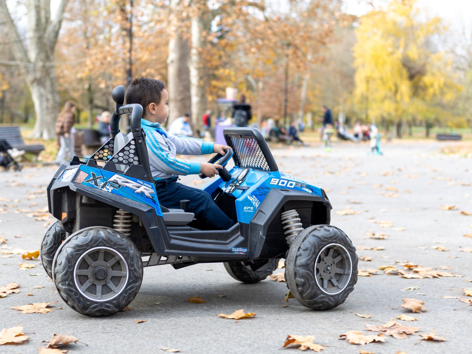 Child steering a battery-powered ride-on toy car outdoors in a park