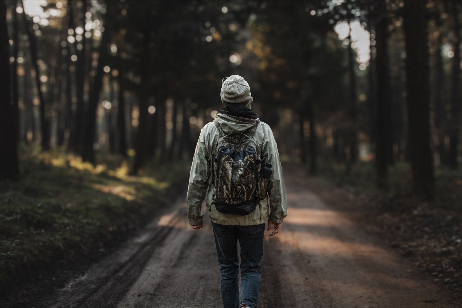 Hiker with a backpack walking a dirt forest trail, the kind of tick and mosquito habitat DEET and picaridin are built for