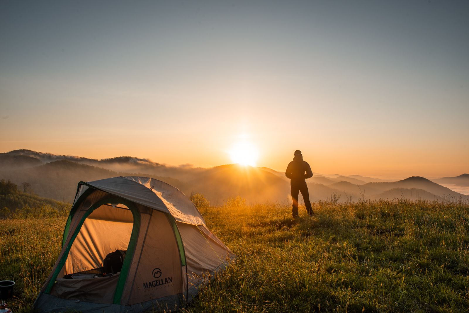 Camping tent pitched outdoors at dusk with a person nearby