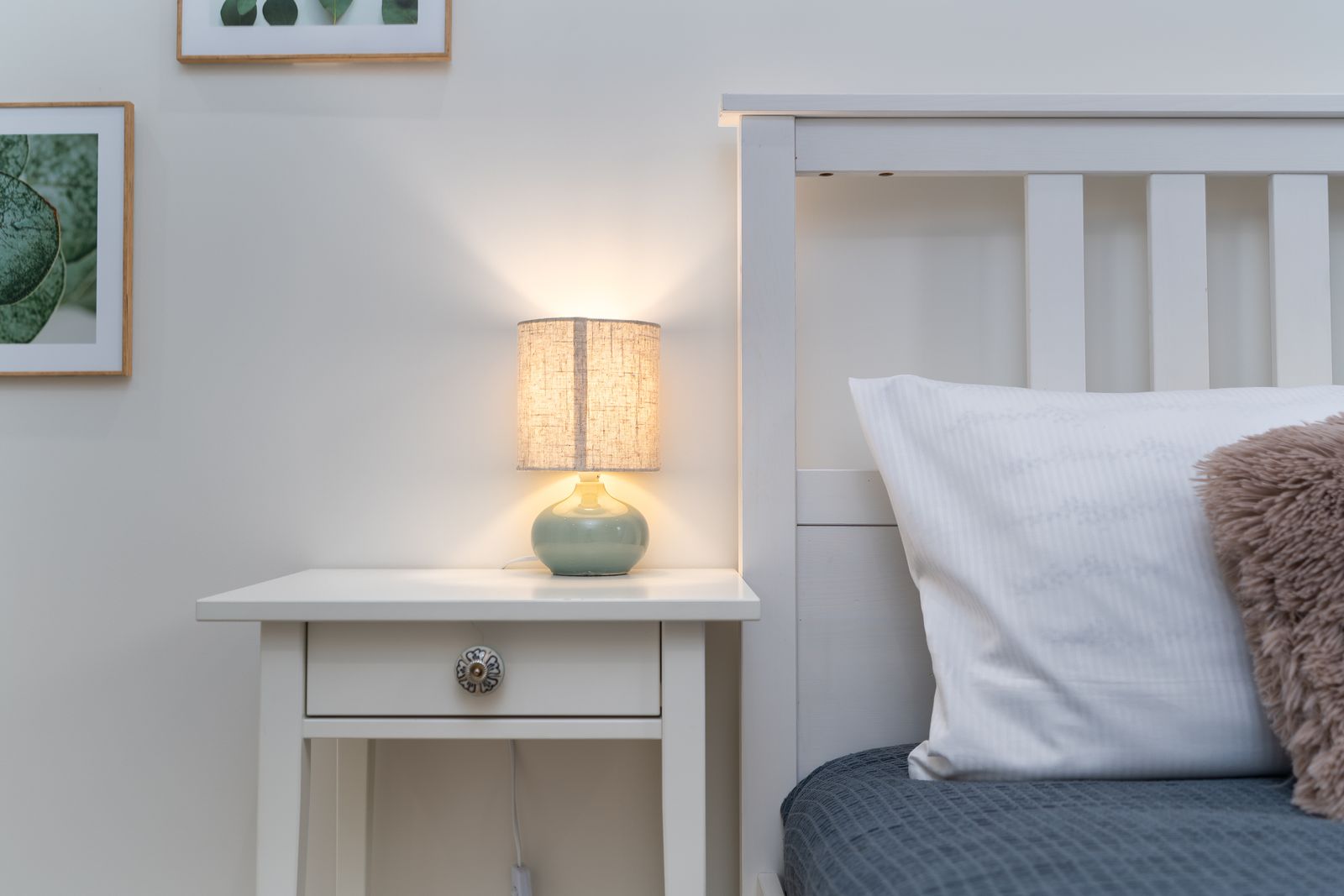 Cozy bedroom with a lit lamp on a white nightstand beside the bed at night