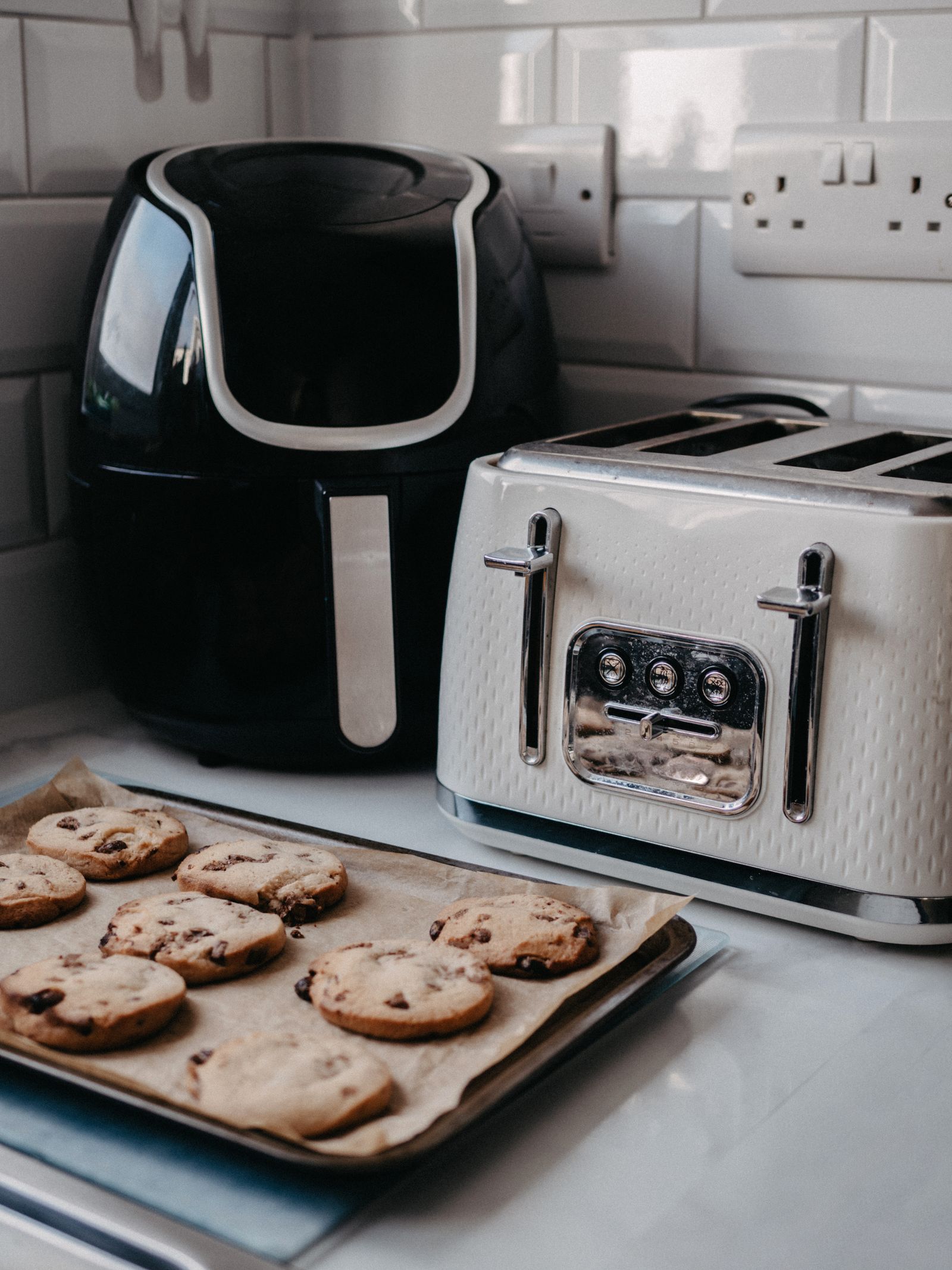 Air fryer and toaster on a modern kitchen counter beside a tray of freshly baked cookies