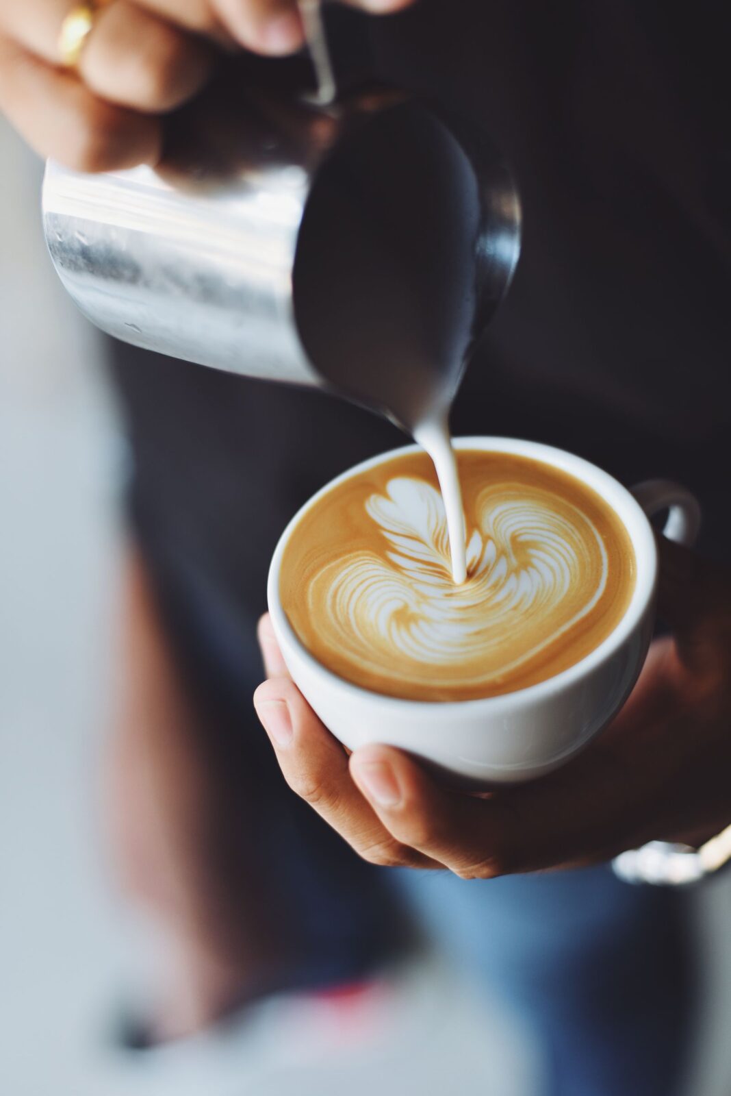 Person pouring frothed milk into a cup of coffee at home