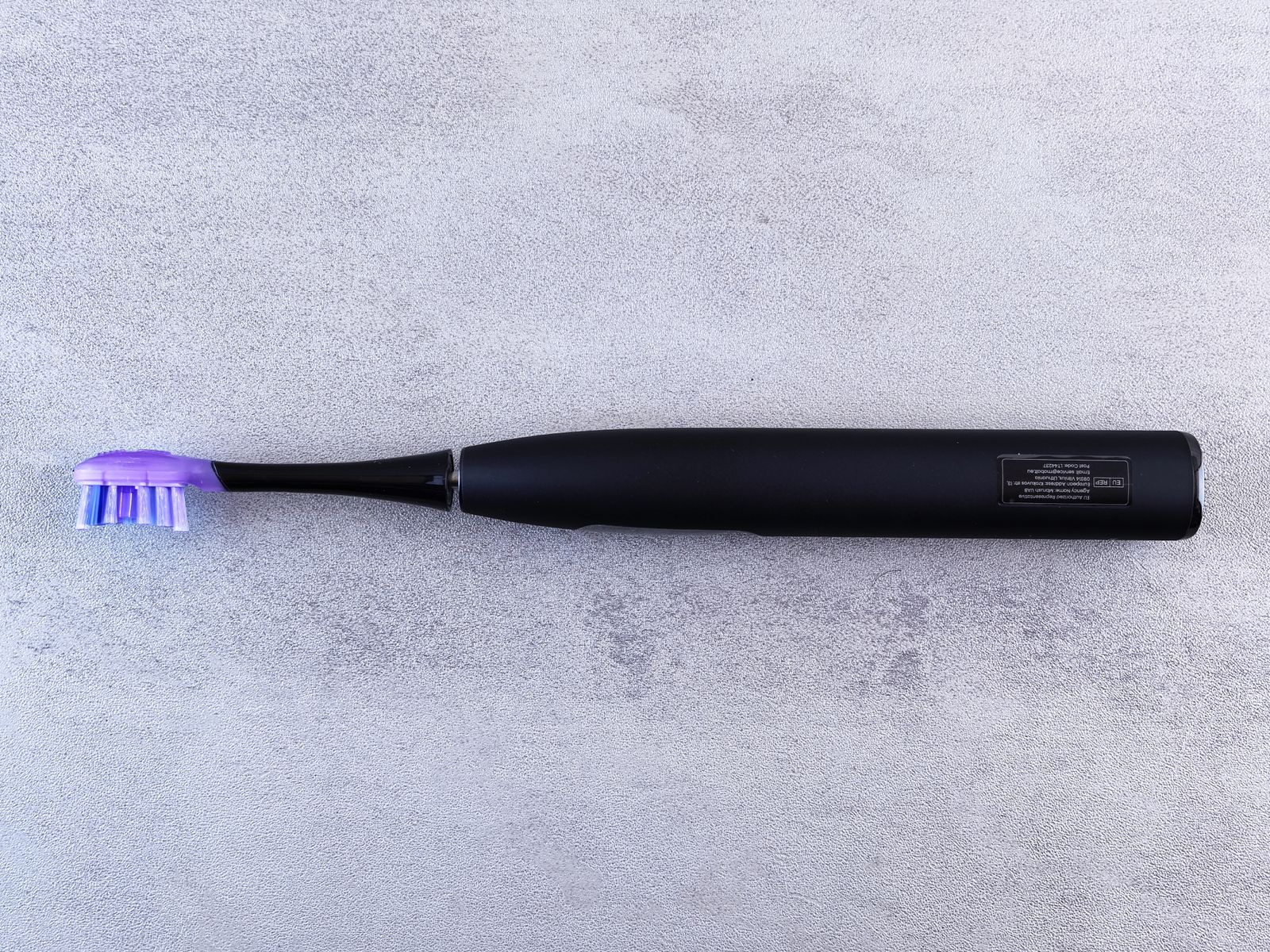 Black electric toothbrush with a purple brush head lying on a concrete surface