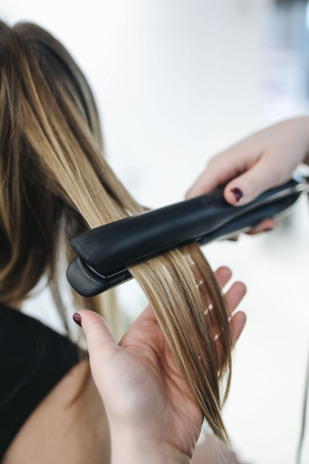 Close-up of a person straightening a section of hair with a heated styling tool
