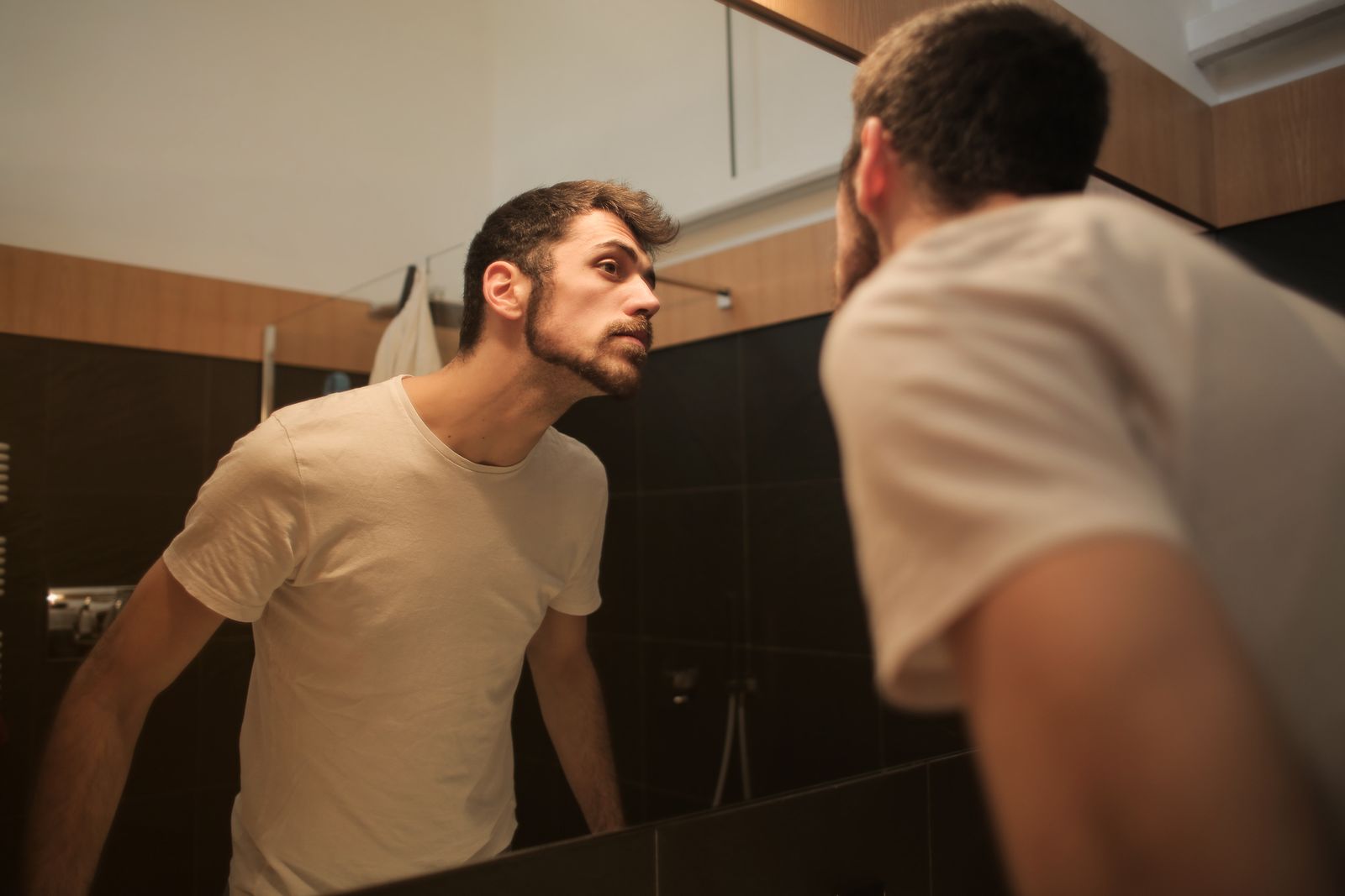 Man closely checking facial detail in a bathroom mirror during a grooming routine