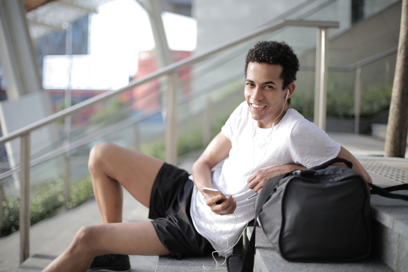 Young man in wireless earbuds resting after a workout on city stairs