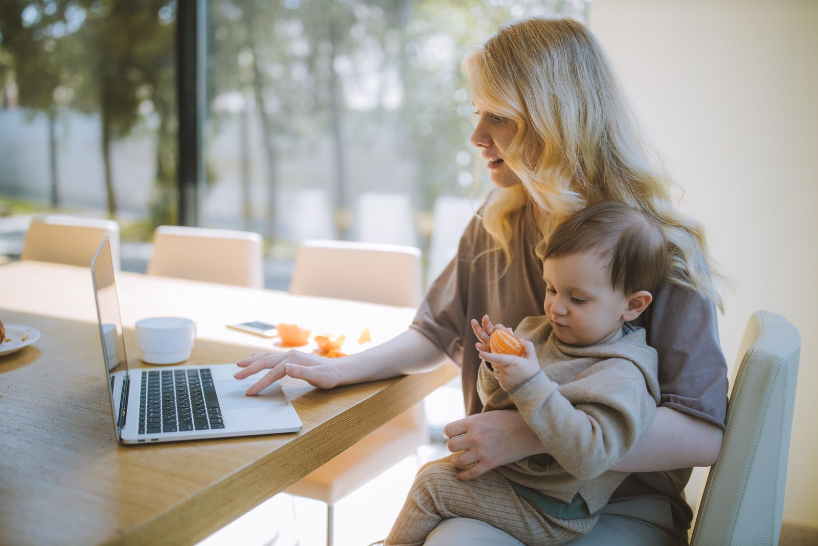 A parent working on a laptop while carrying a baby