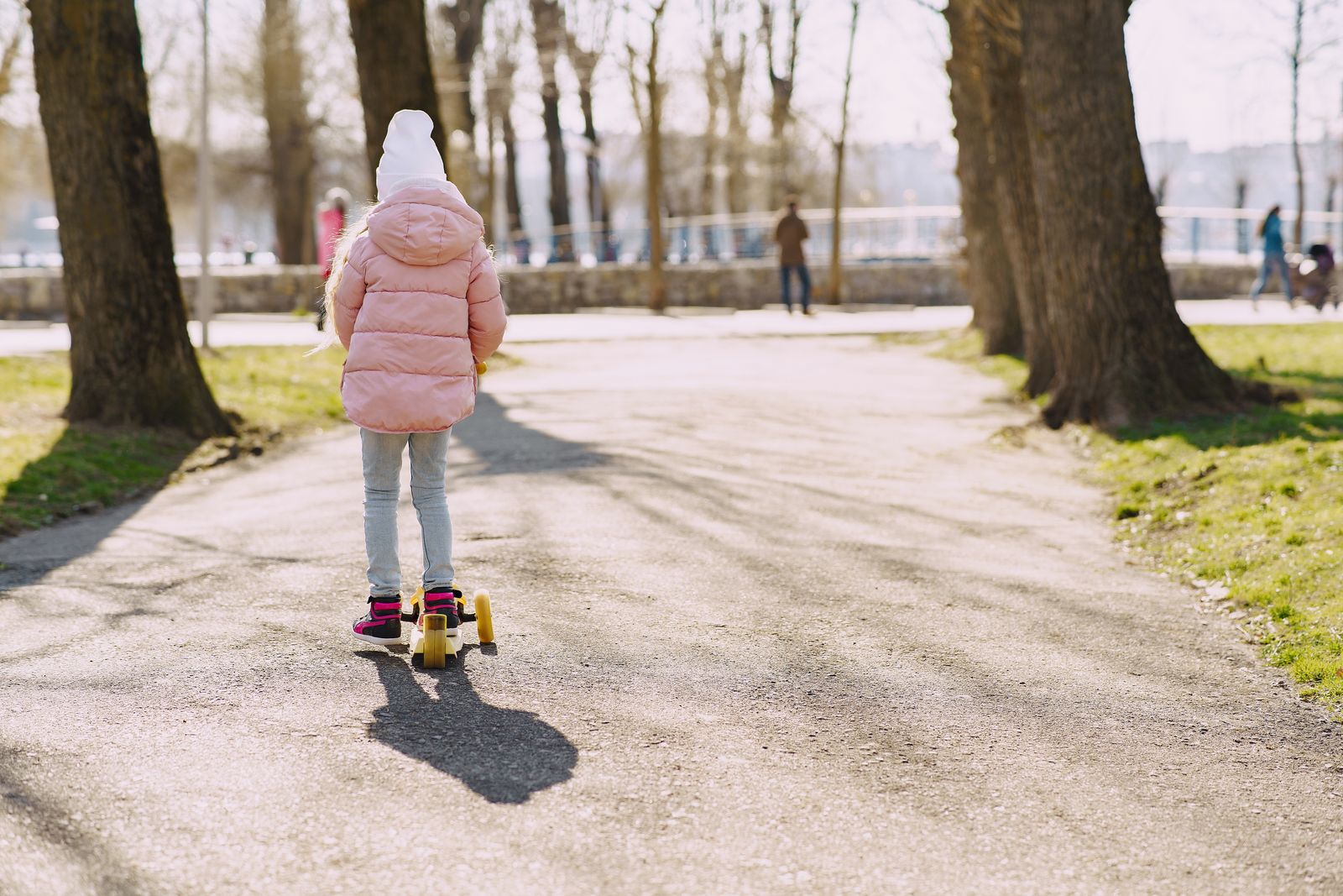 Child riding a kick scooter on a park path