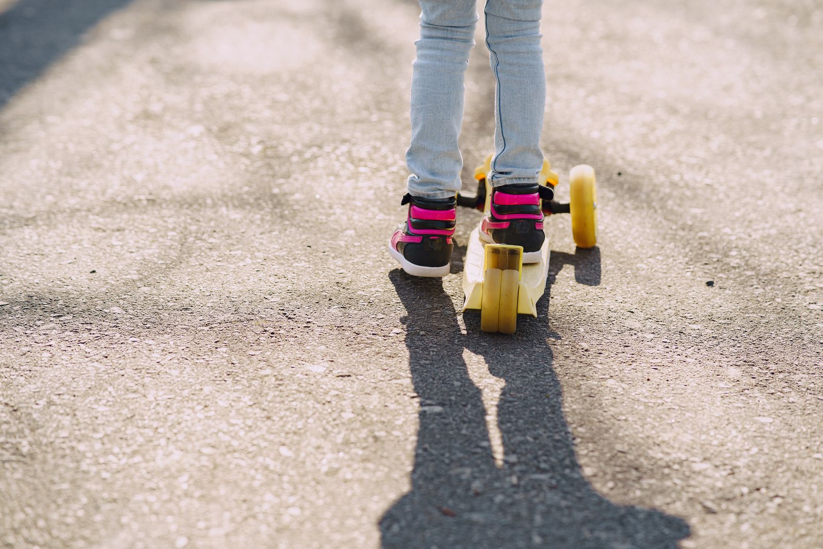 Young child riding a kick scooter along an asphalt path