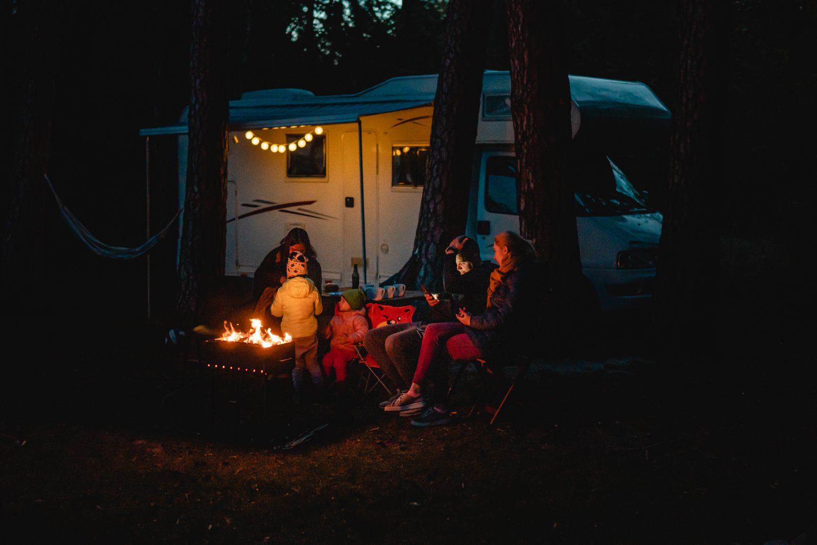 People sitting on camping chairs near a campfire