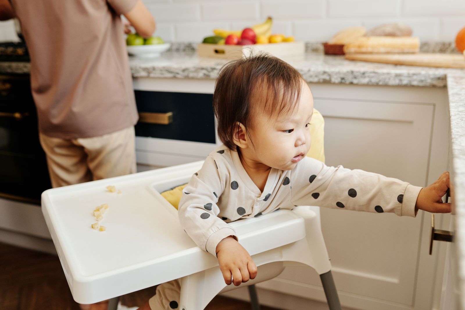 A baby sitting in a high chair in the kitchen near the table