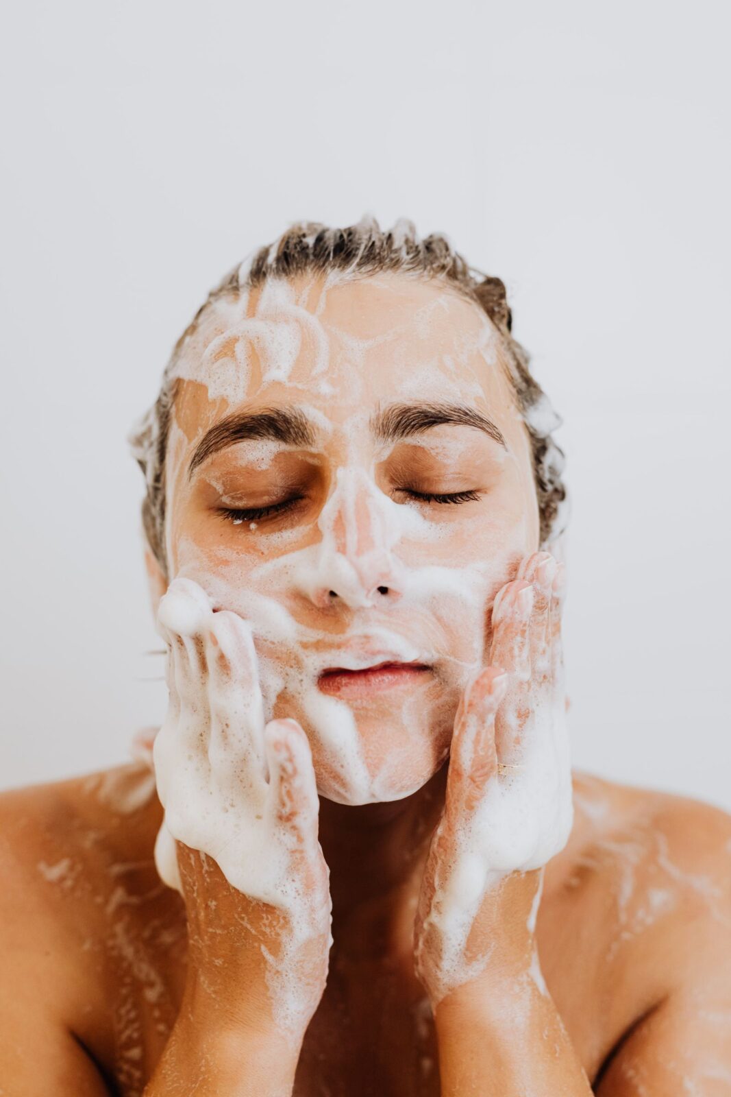 A woman washing her face with cleanser at a bright sink