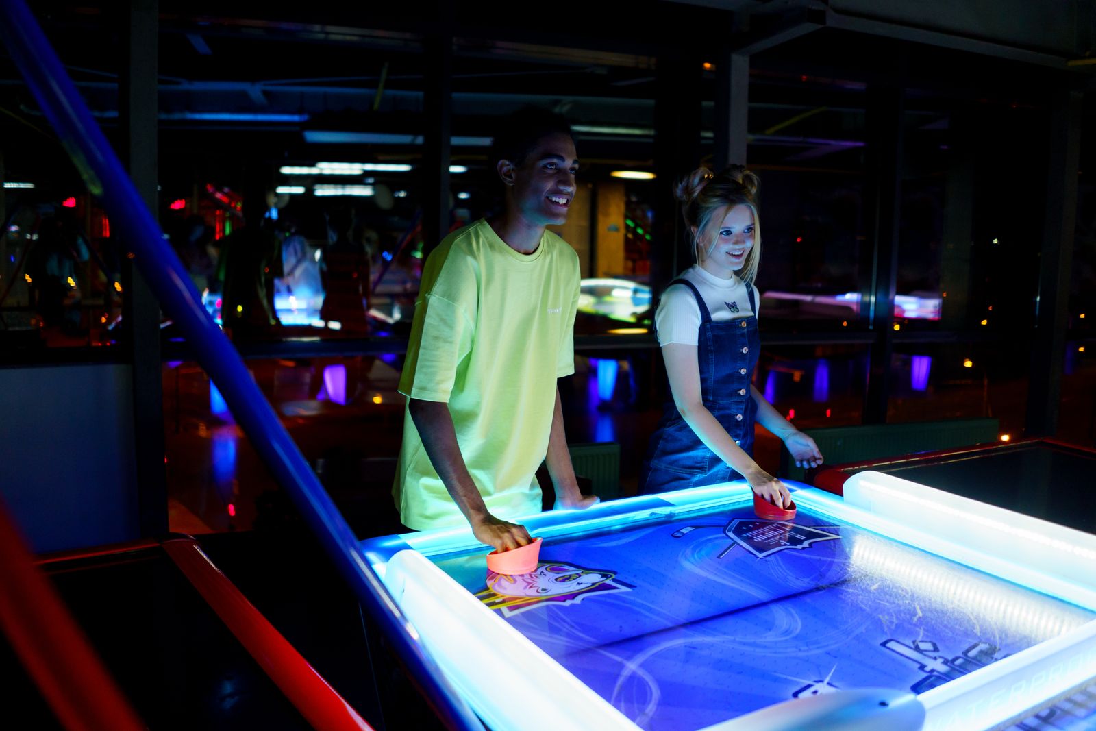 Two people playing air hockey at a table lit up with neon rail lighting