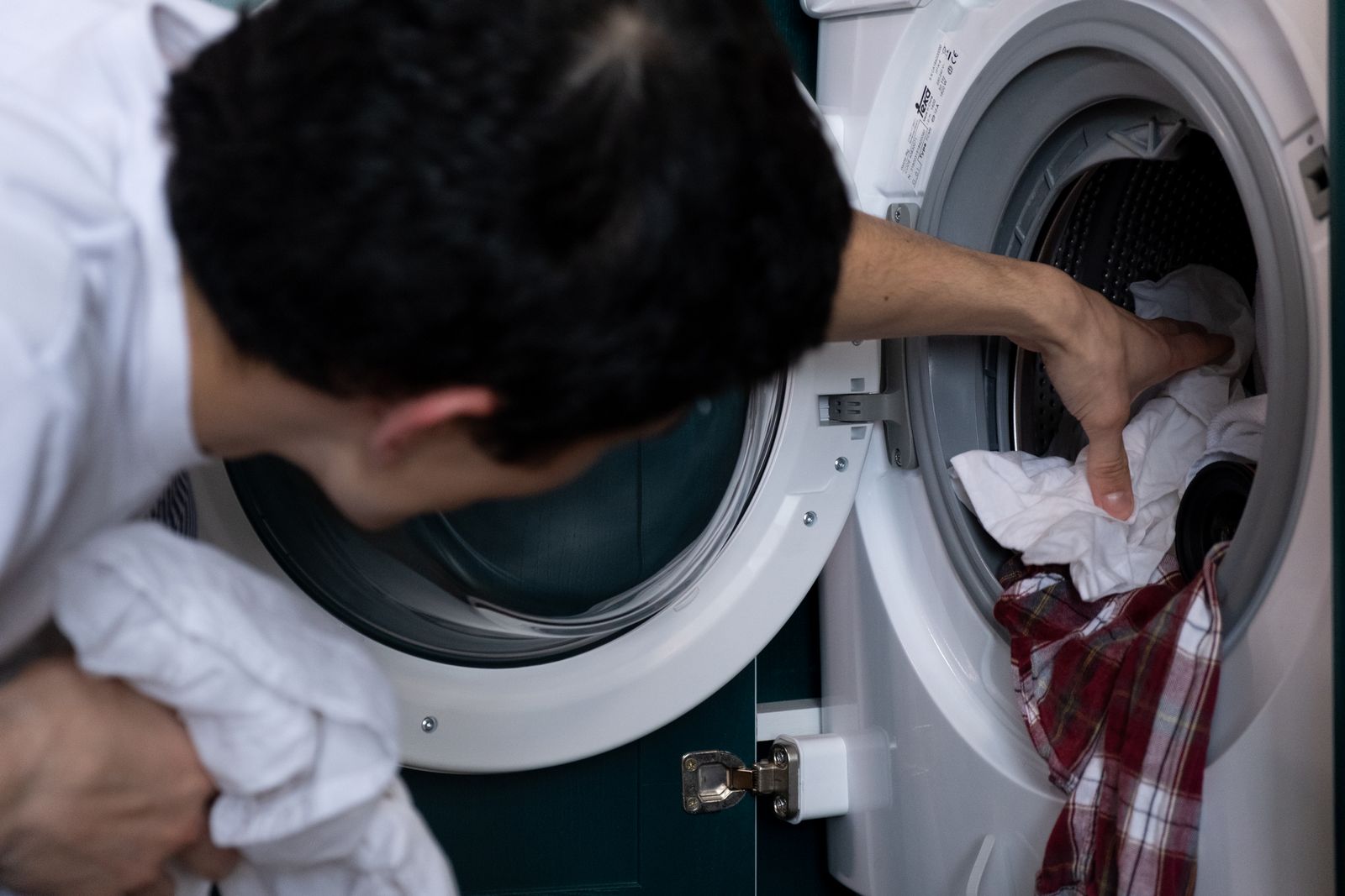 Person unloading clean laundry from a front-loading washing machine — detergent sheets vs pods vs liquid comparison hero