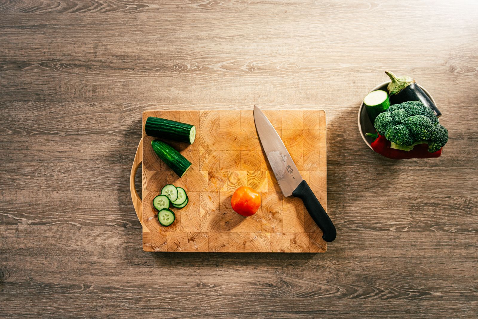 A sharp chef's knife beside freshly sliced vegetables on a wooden board