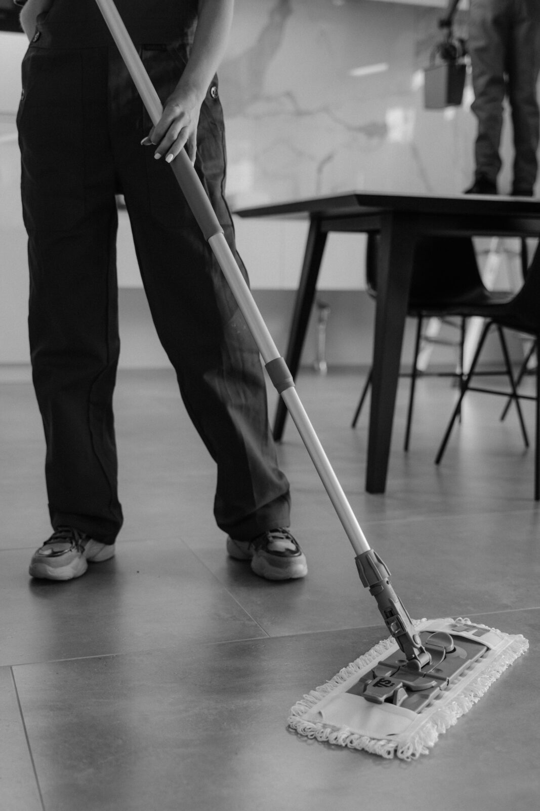 A 2-in-1 robot vacuum and mop cleaning tile beside its self-washing dock