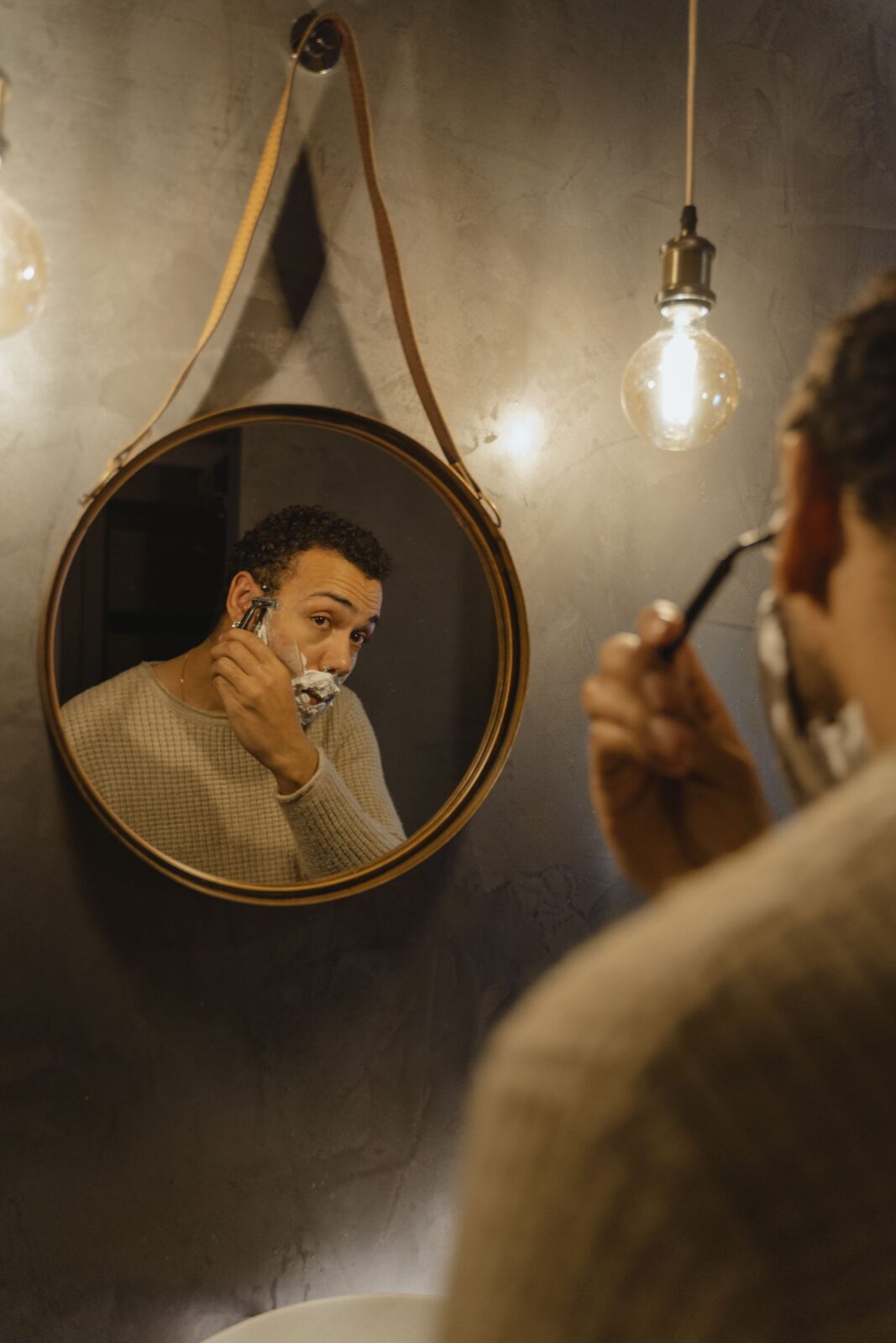 Man grooming at a bathroom mirror, representing the routine upkeep a nose and ear hair trimmer is used for