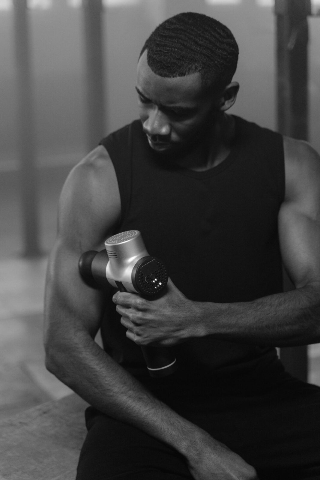 A fit man using a massage gun on his leg muscles