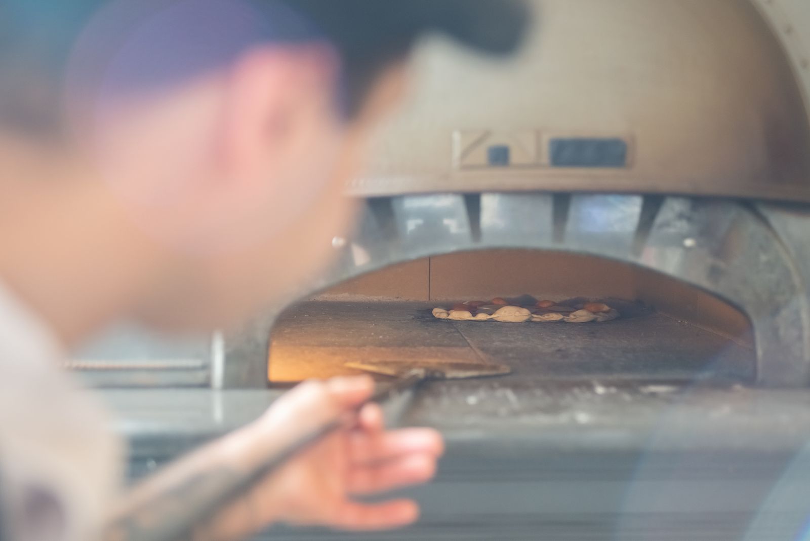 Person tending a pizza cooking inside a fired oven