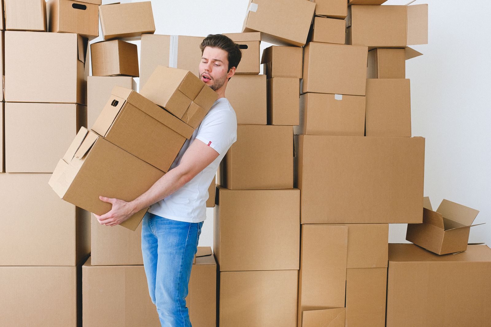 Young person carrying cardboard moving boxes into a new room