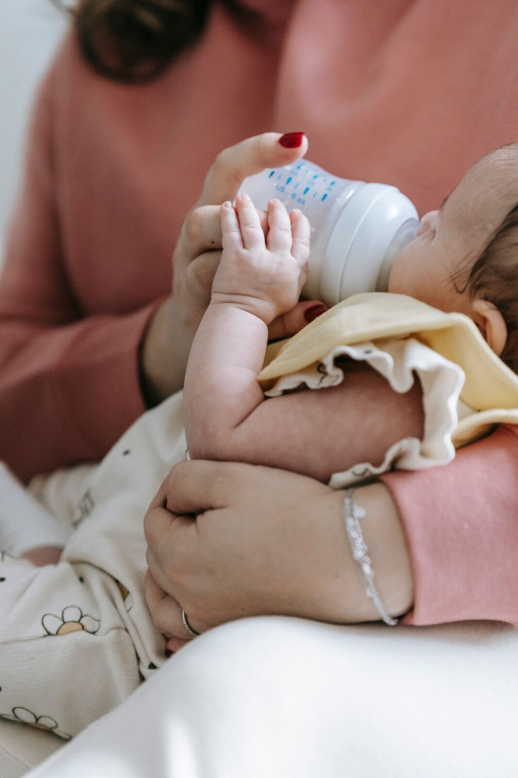A parent gently bottle-feeding a calm newborn