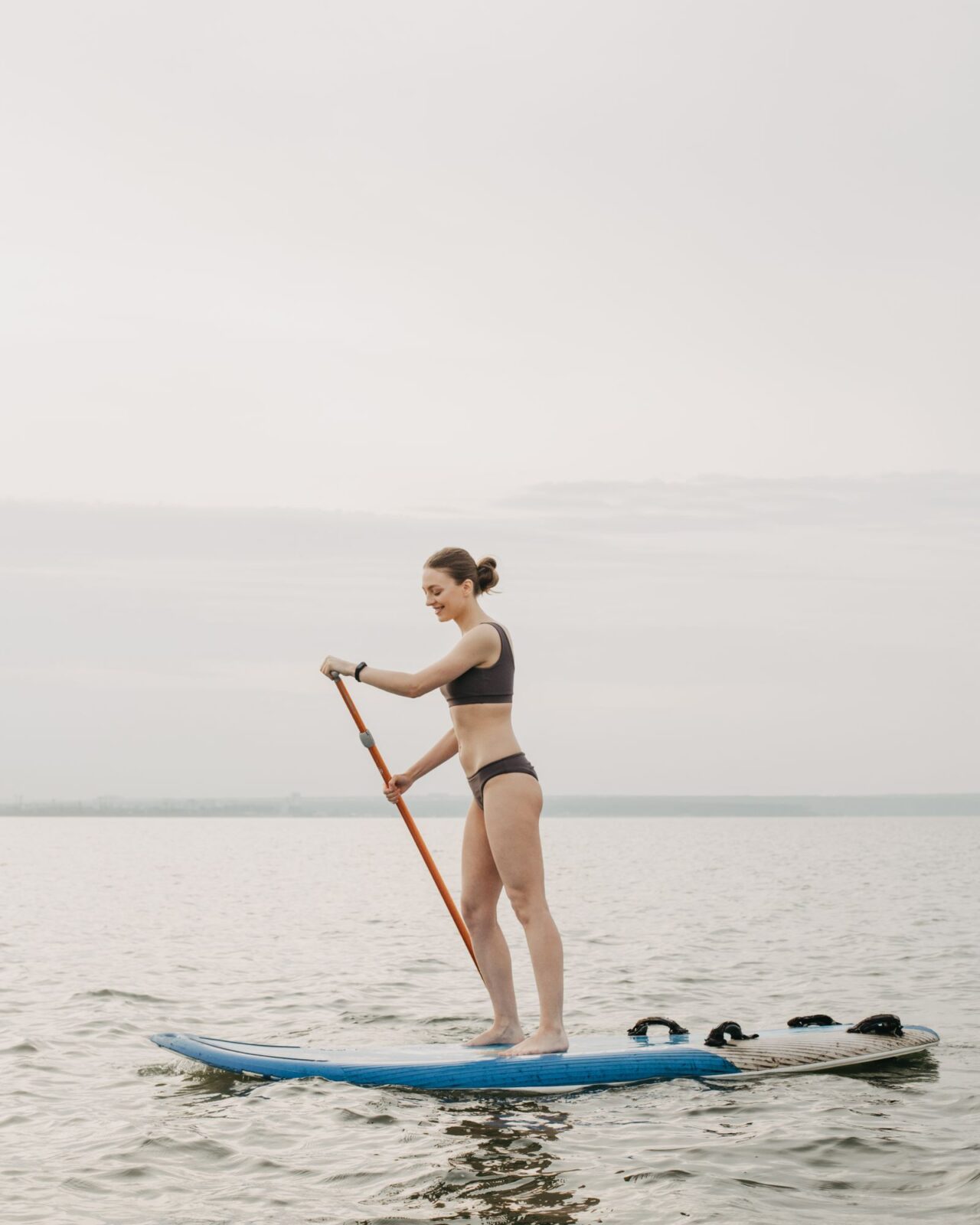 Paddler standing on a SUP crossing calm glassy water in summer