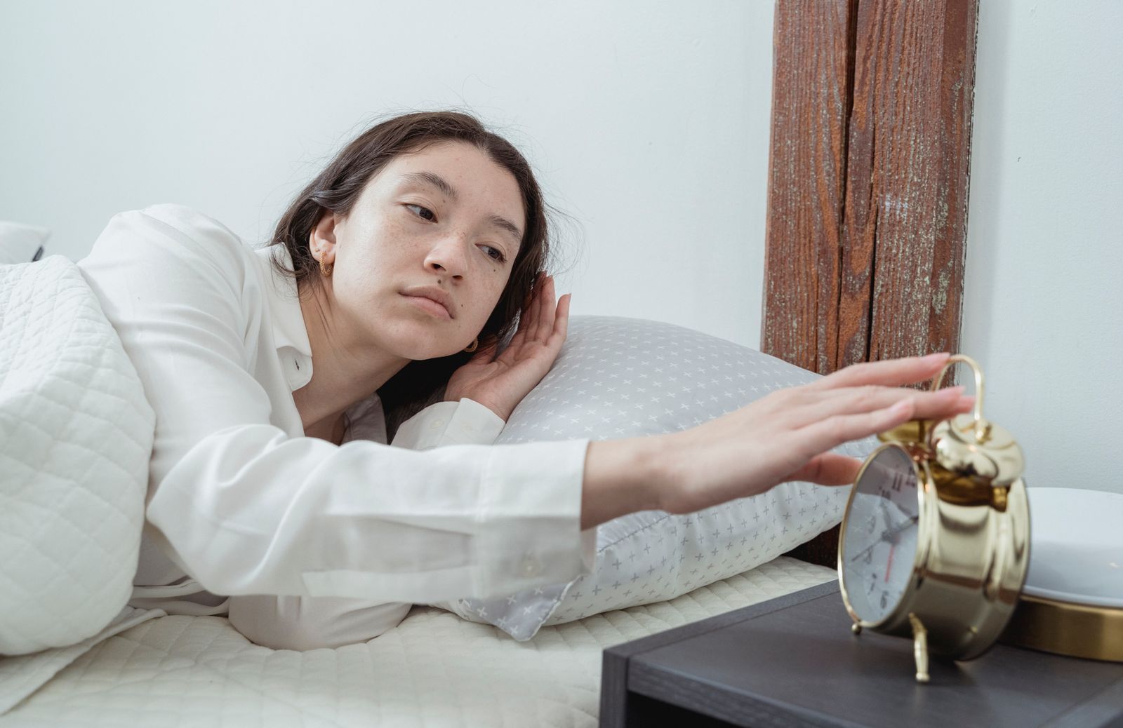 Woman waking up beside a bedside alarm clock in soft morning light — sunrise alarm clock comparison hero
