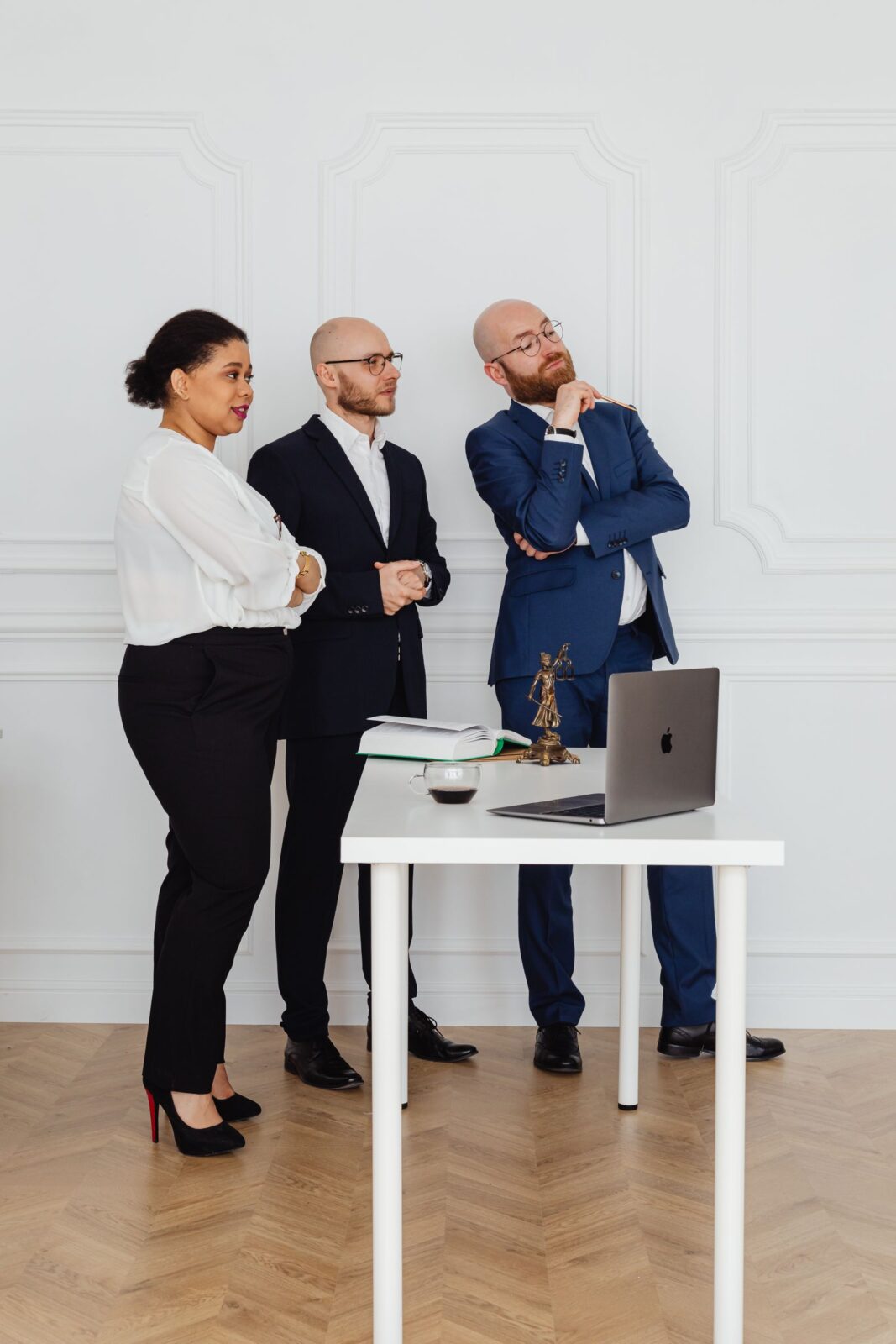 Coworkers standing around an adjustable desk workstation with a laptop, representing desk exercise equipment used while working