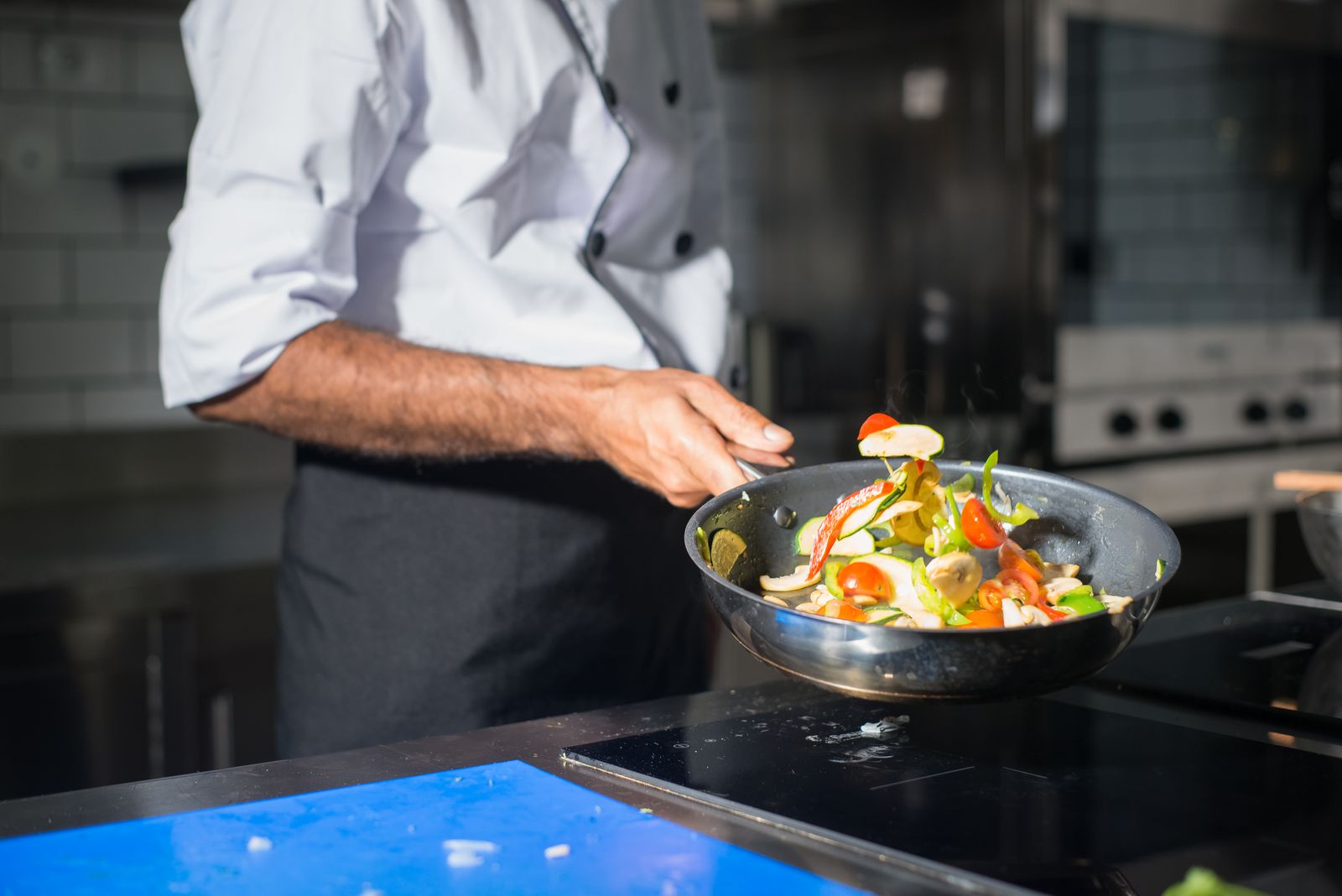 A carbon steel skillet tossing vegetables over a flame