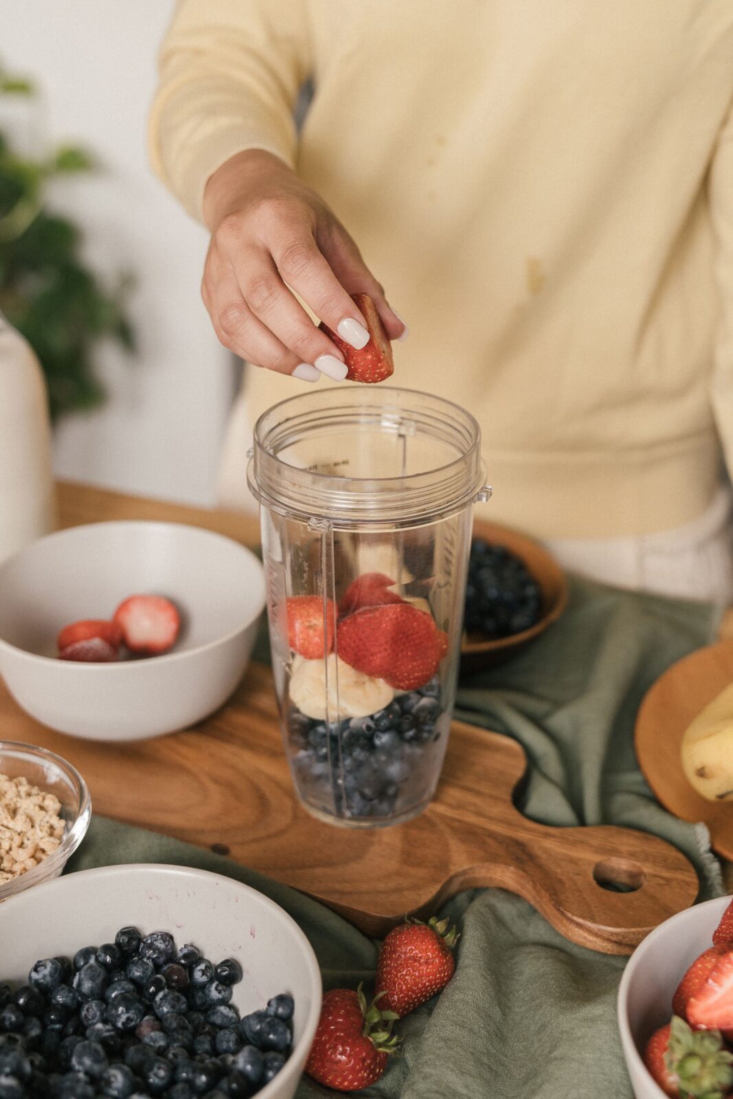 A person putting fresh fruit into a blender jar