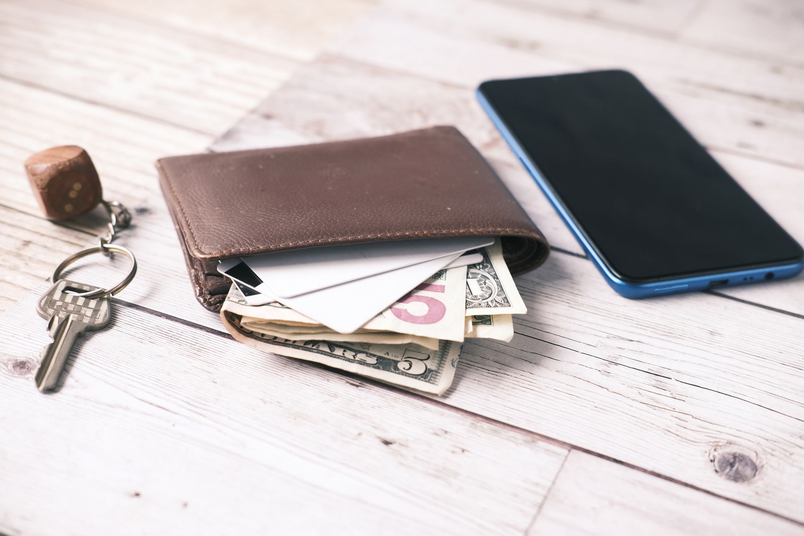 Wallet, cash, smartphone, and keys laid out on a wooden surface