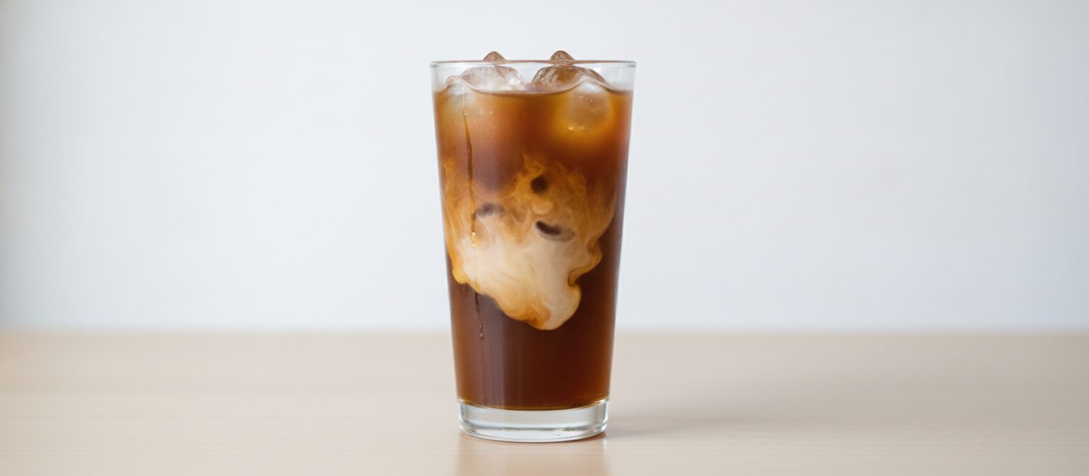 A tall glass of iced cold brew coffee over ice with a swirl of cream