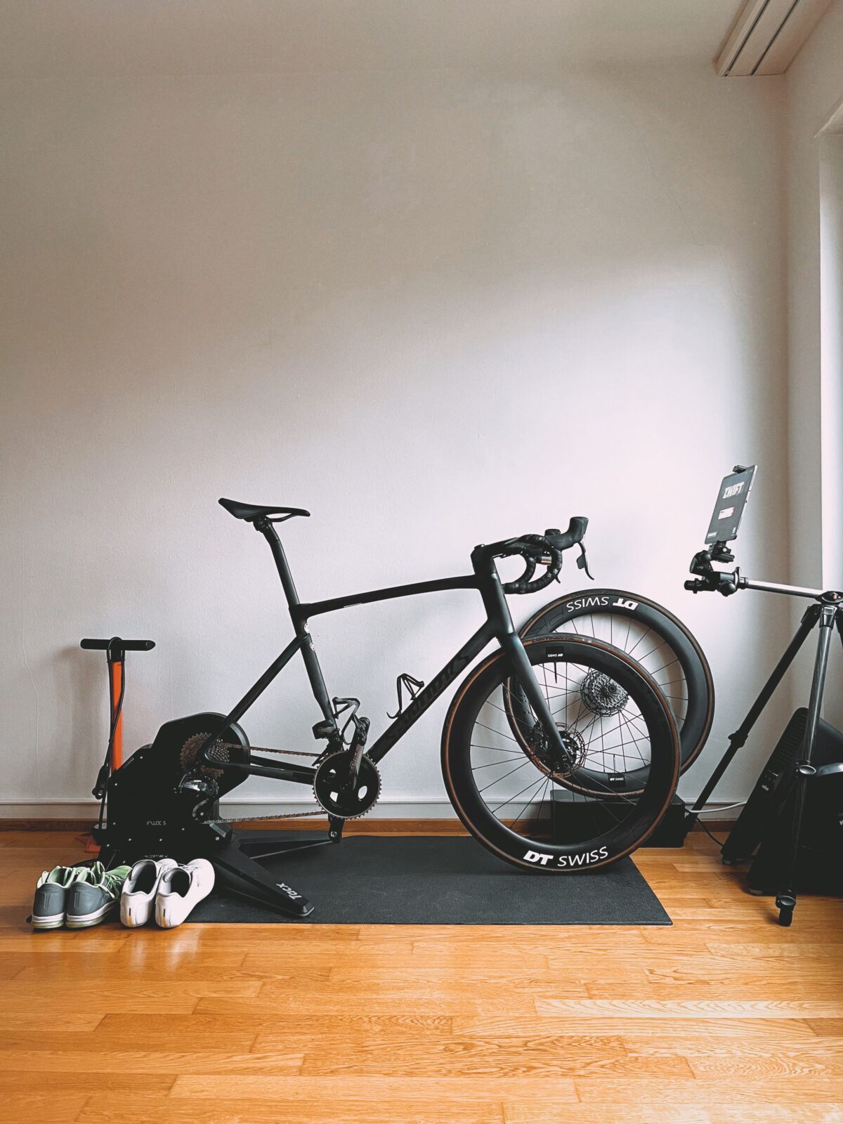 A sleek black road bike mounted on a stationary bike trainer in a minimalist indoor setup