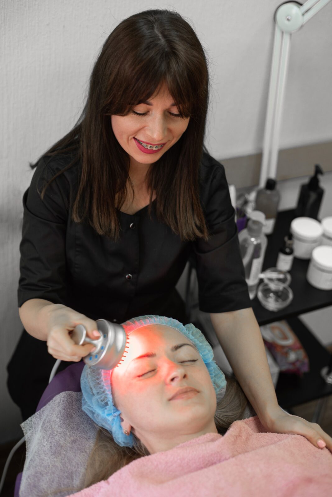 A woman lying down receiving red LED light therapy treatment on her face in a clinic setting