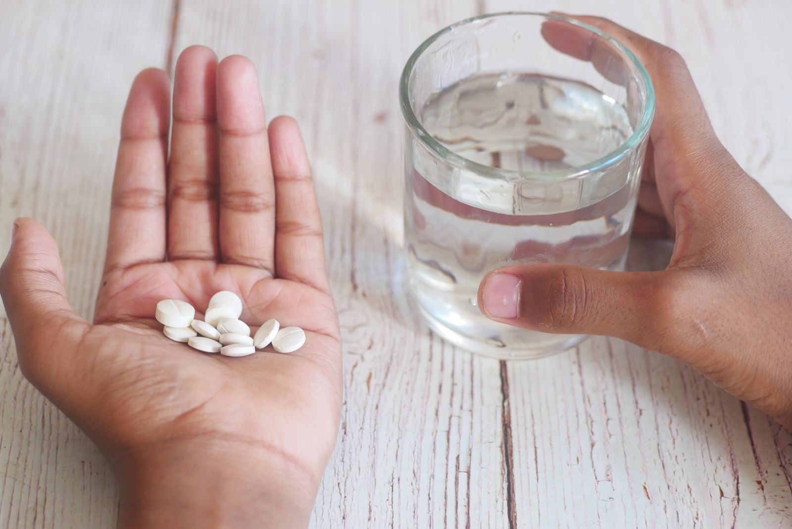 A hand holding white pills next to a hand holding a glass of water