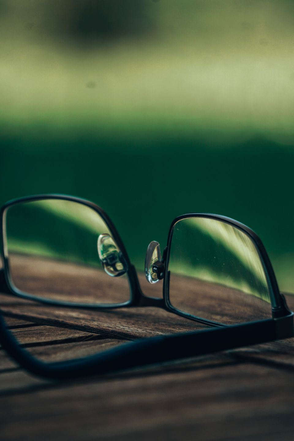 Close-up of eyeglasses on a wooden table with blurred green background