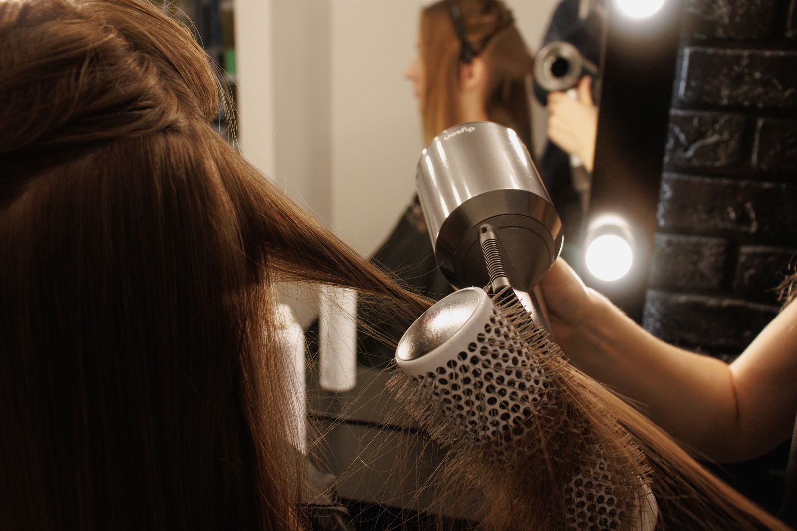 Stylist blow-drying a section of hair with a round hot-air styling brush