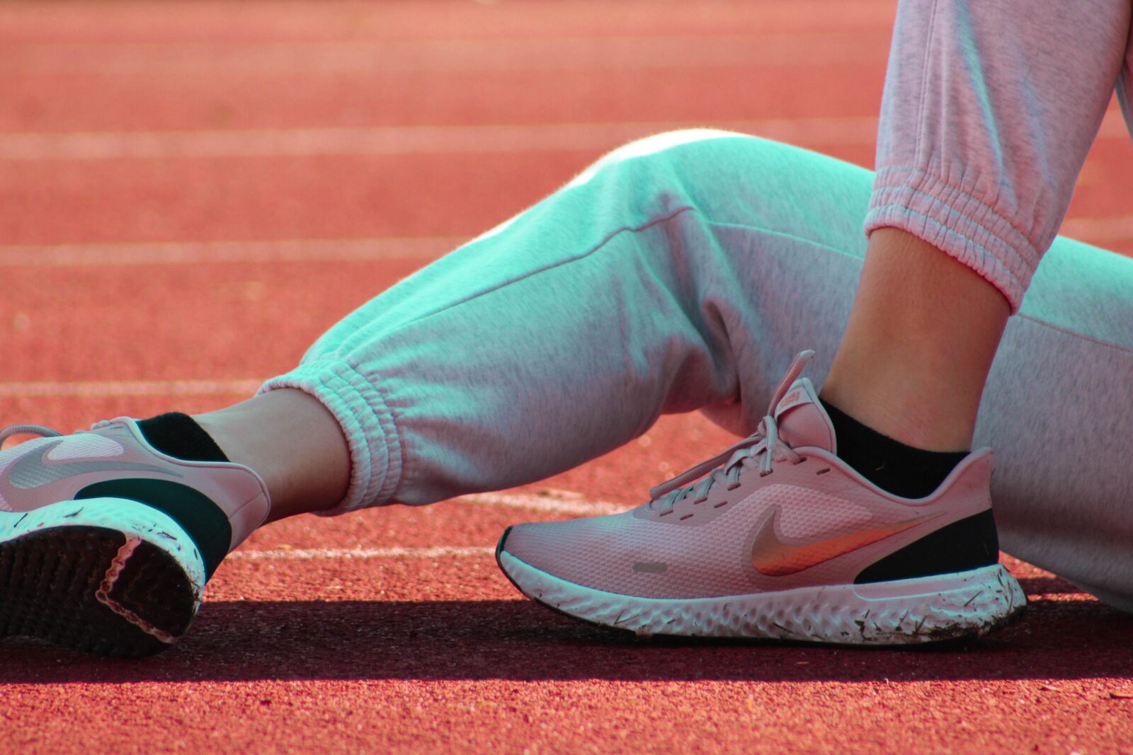 An athlete's legs and feet resting on a running track in warm sunlight