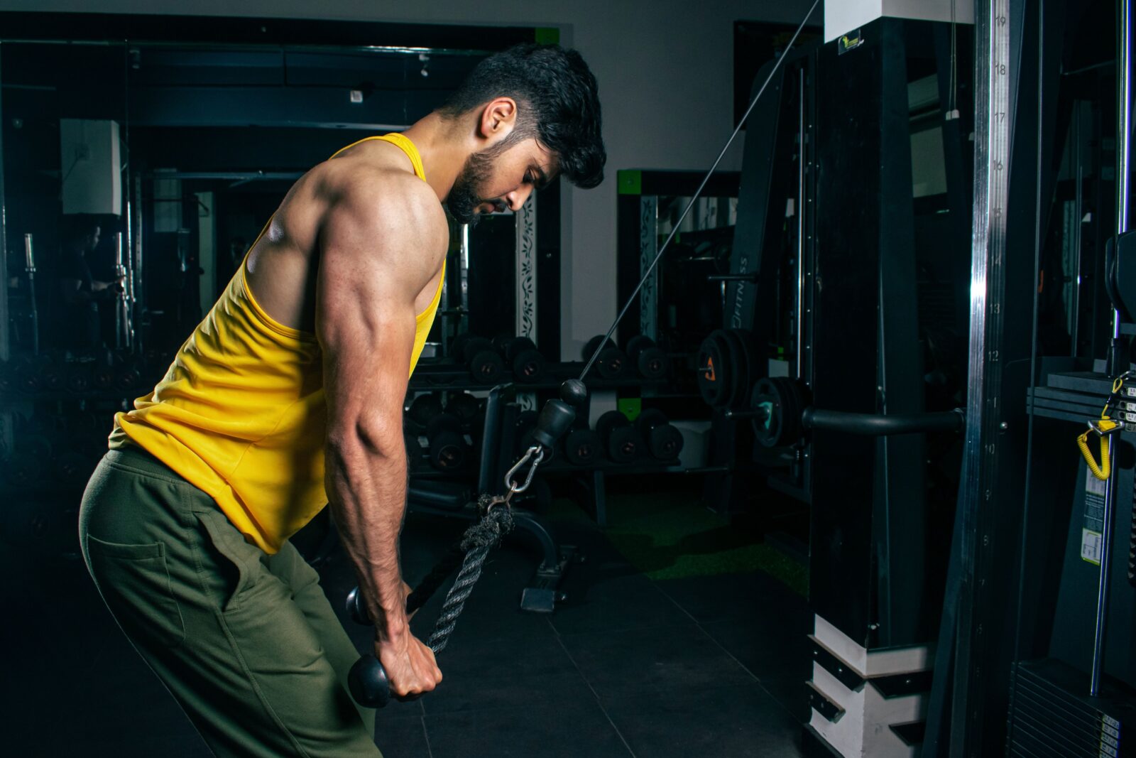 A man in a yellow tank top performing an upper body exercise on a cable machine