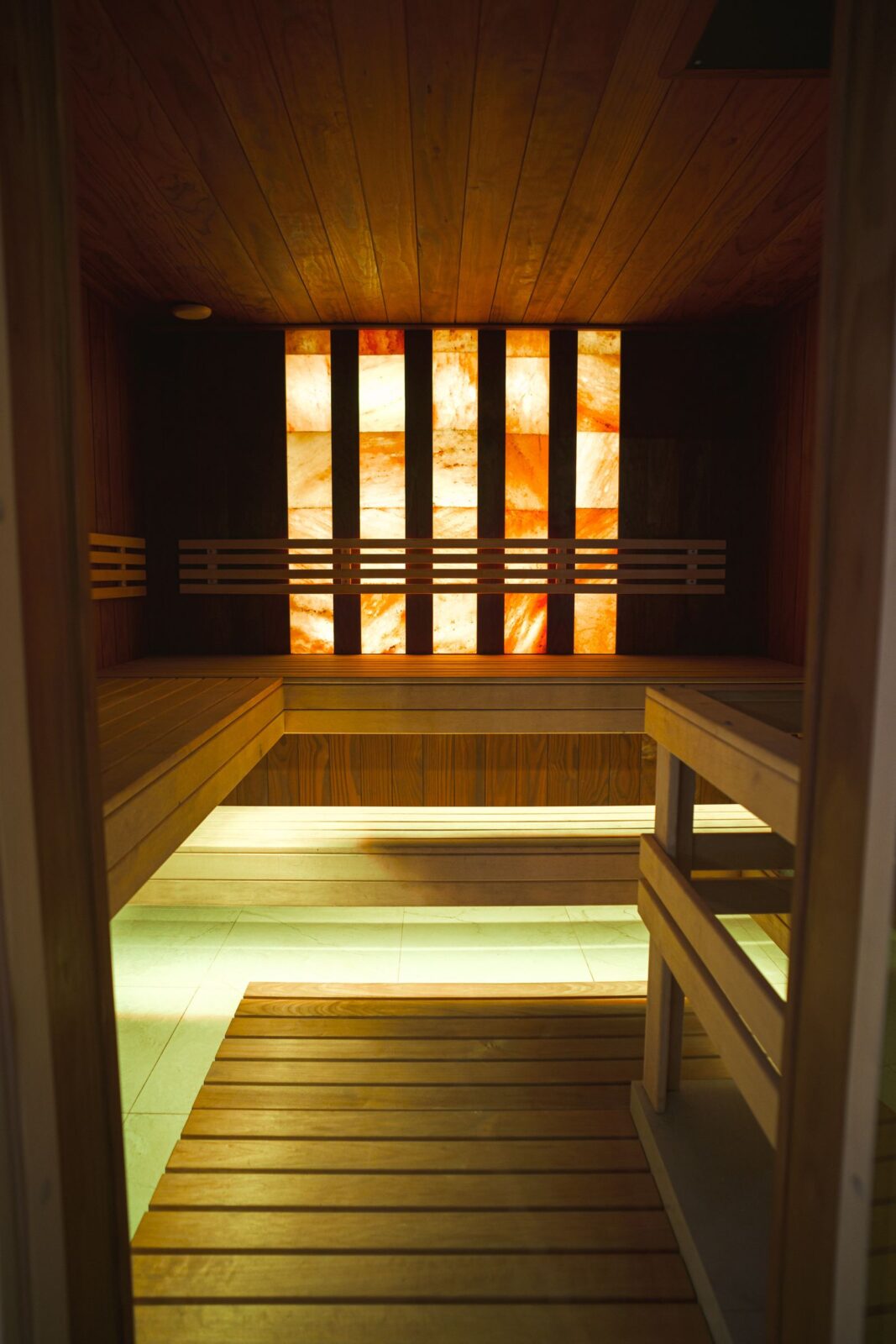 Wooden walk-in sauna room with benches and glowing salt wall panels