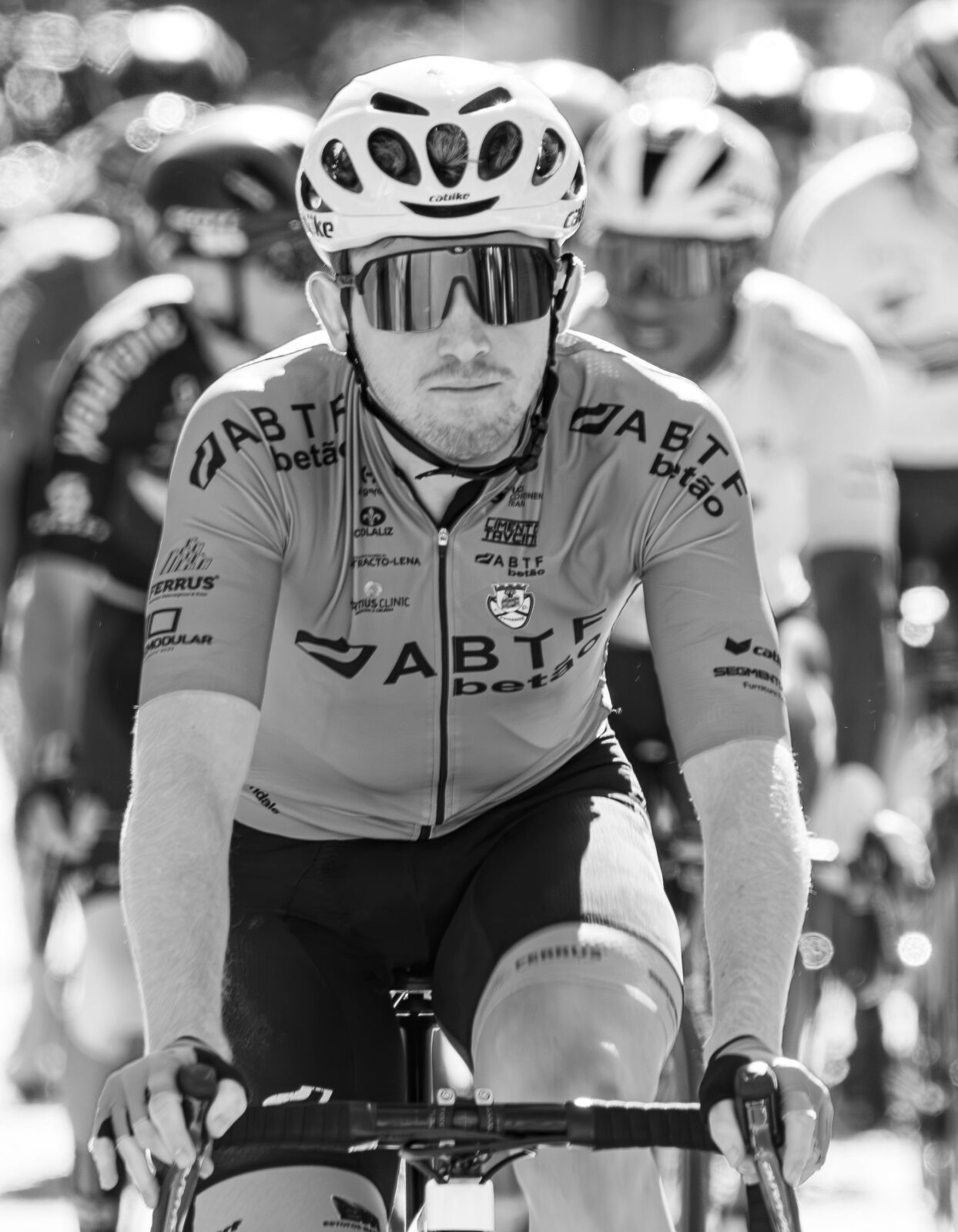 Black and white photo of a cyclist wearing a helmet and sunglasses during a race