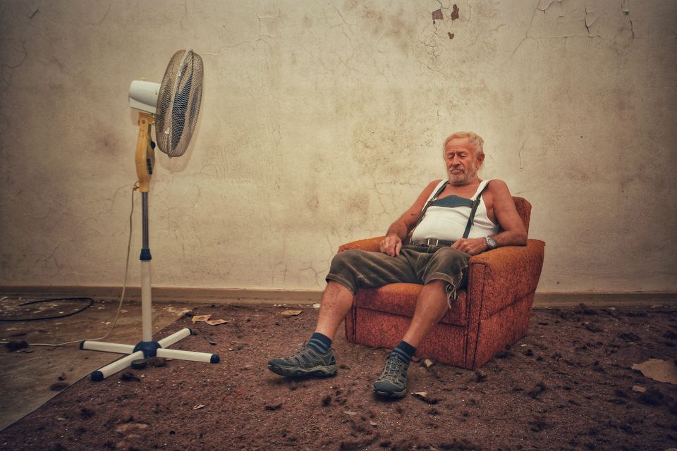 Elderly man resting in an armchair with a fan in a rustic indoor setting