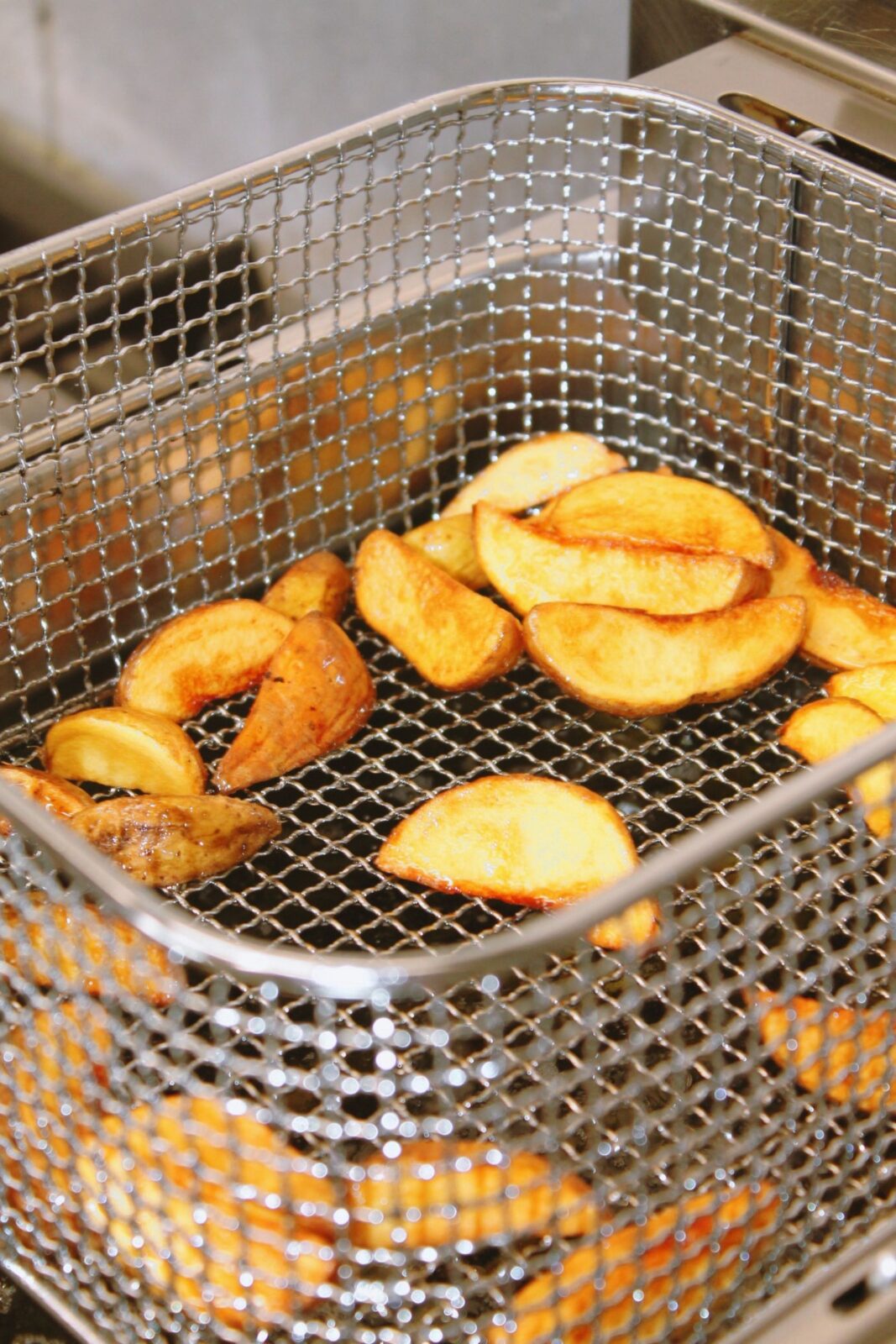 Golden brown fried potato wedges in a stainless steel mesh basket