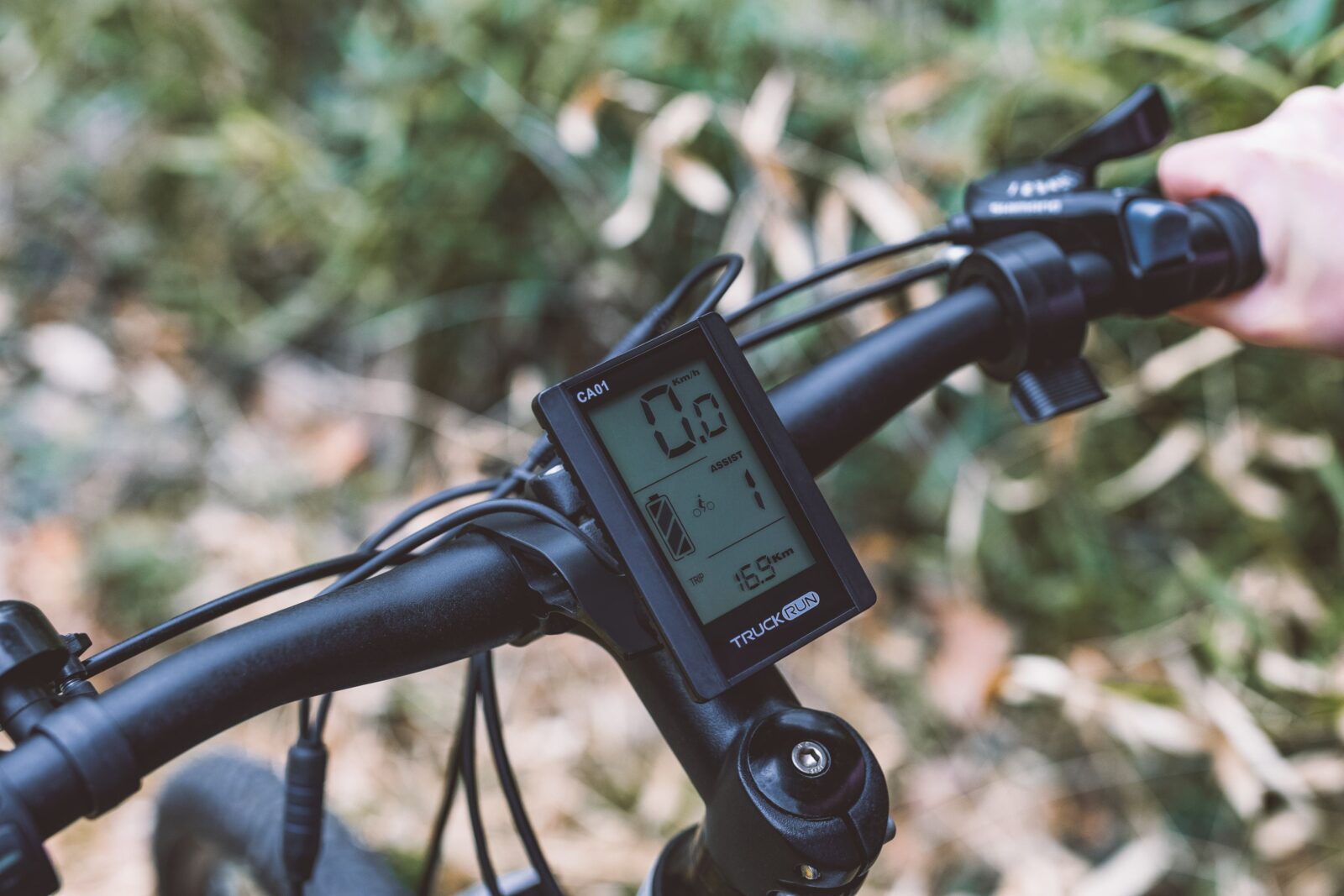 A detailed view of bicycle handlebars with a digital display screen against an autumn backdrop